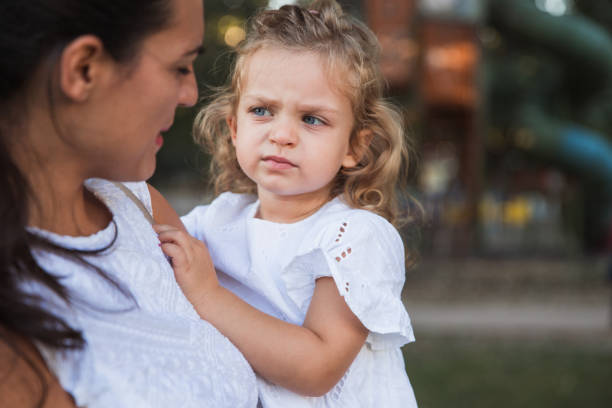 Outdoors image of a Serious latino six years old little girl posing with her mother in the background