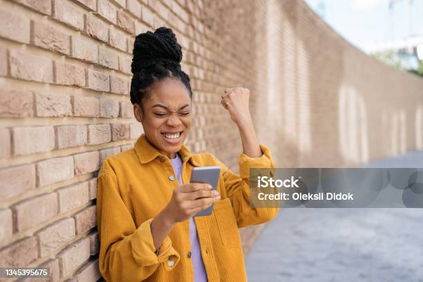 Emotional African American Woman Using Mobile Phone Reading Good News About Exam Result Beautiful Happy Female Win Online Lottery Celebration Success Stock Photo - Download Image Now