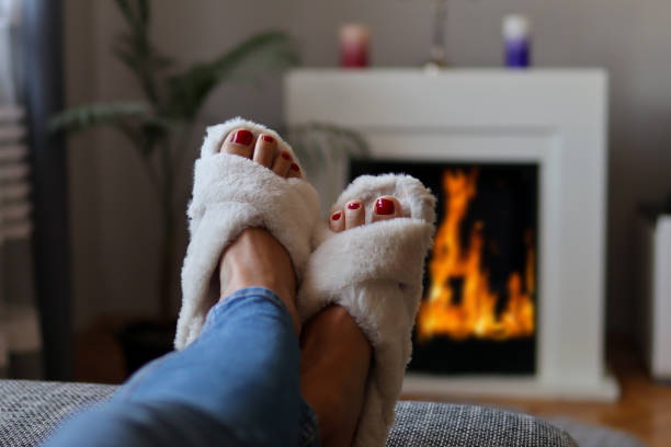 Female feet in slippers warms on fireplace at home stock photo