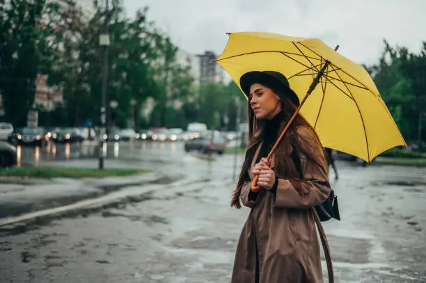 Photo of Beautiful woman holding a yellow umbrella on a rainy day while walking in the city street