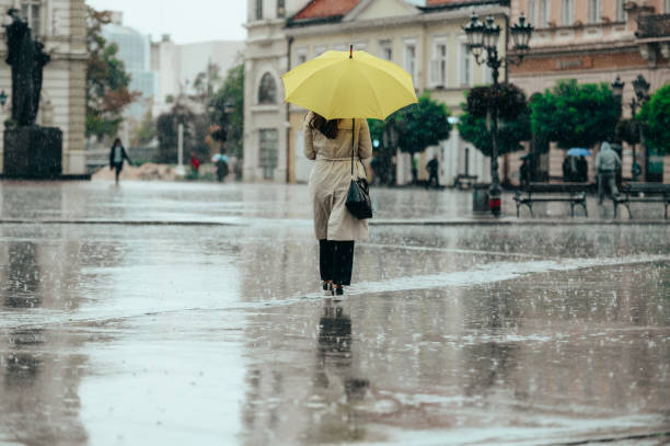kobieta nosząca żółty parasol i spacerująca podczas ulewnego deszczu w mieście - people in a row in a row business office worker zdjęcia i obrazy z banku zdjęć