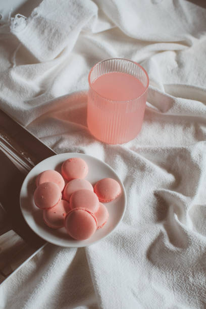 Pink macaron cookies with cup of coffee and rose flowers on white background. Spring still life scene. Vintage pastel styled photo. Copy space for you text. Toned image.