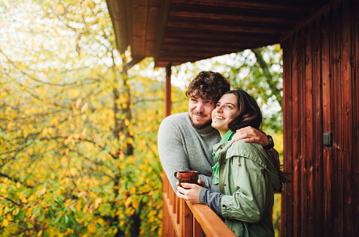 Young hiking couple enjoying a hot drink on the terrace of a wooden lodge.