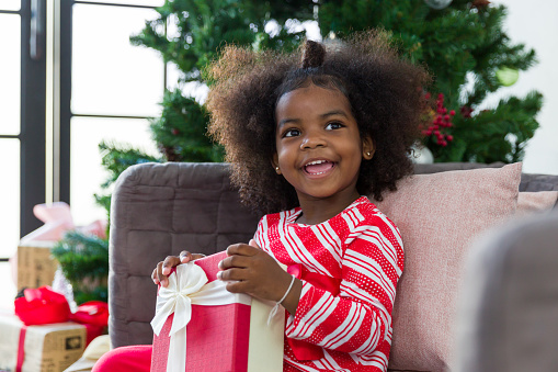 Happy cute African American little smiling girl with Christmas gift box or presents gift on Christmas at home. Christmas holiday celebration, Merry Christmas and Happy Holidays