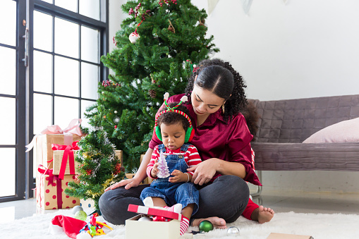Happy family on Christmas holiday. African American mother and little son playing with decoration items for Christmas tree at home. Merry Christmas and Happy Holidays