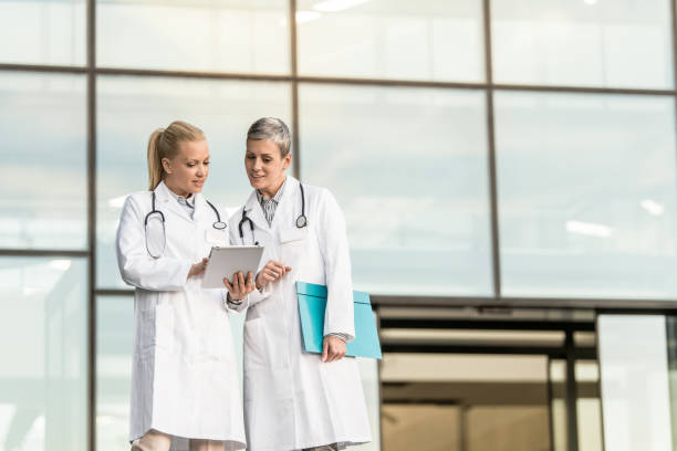istock Two happy female doctors using digital tablet while standing in front of hospital. 1345419646