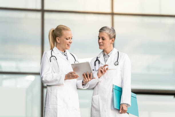 istock Two happy female doctors using digital tablet while standing in front of hospital. 1345419681