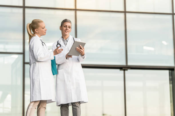 istock Two happy female doctors using digital tablet while standing in front of hospital. 1345419760