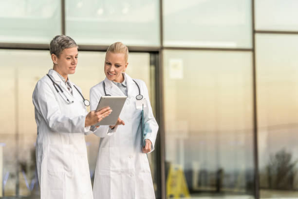 istock Two happy female doctors using digital tablet while standing in front of hospital. 1345420941