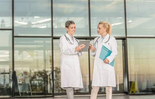 istock Two happy female doctors using digital tablet while standing in front of hospital. 1345420953