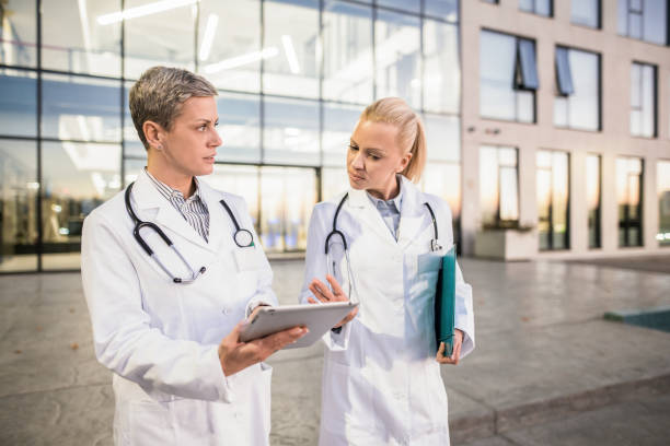 istock Two female doctors using digital tablet while walking in front of hospital. 1345421048