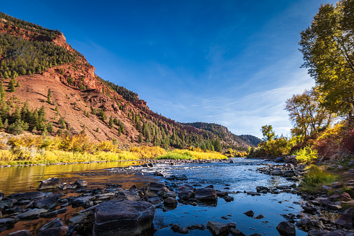 black water mountain river with full fall color, red cliff background, and sunrays