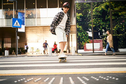 15-year-old asian teenager boy skateboarding outdoors in the street
