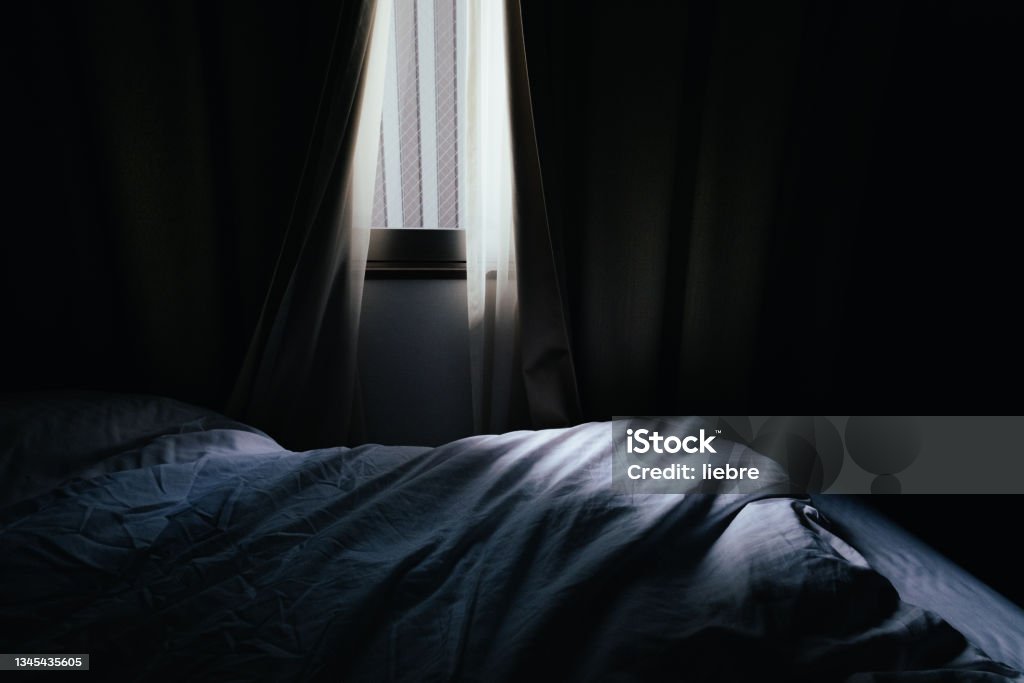 Image of a bedroom where light shines through the gaps in the curtains Dark Stock Photo
