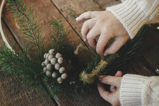 istock Hands making modern christmas wreath on rustic table with fir branches, brunia herb, round wooden hoop. Atmospheric moody image. Winter holidays preparation close up 1345444867