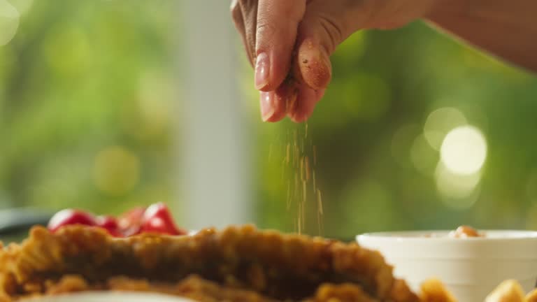 Pouring spice, red pepper on fried meat. Cooking traditional full English breakfast close-up. National British cuisine, french fries, fish and chips. American pub or cafe, fast food