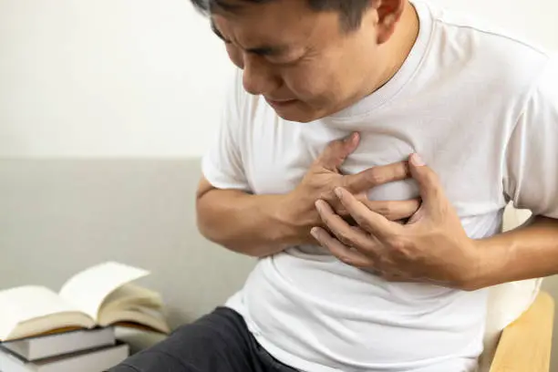 Photo of Asian middle-aged man touching his chest,suffocation and chest pain and tightness,sick male patient with heart or asthma attack,shortness of breath or panic disease problems with breathing,respiratory