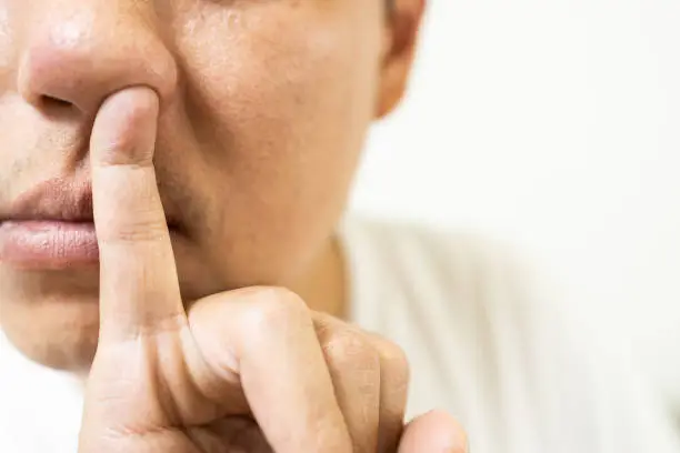 Close-up,little finger inserted inside the nose,pinkie poked into the nostril,asian middle-aged man picking snot with fingertip,itching in the nasal cavity,avoid touching with dirty hand,health care