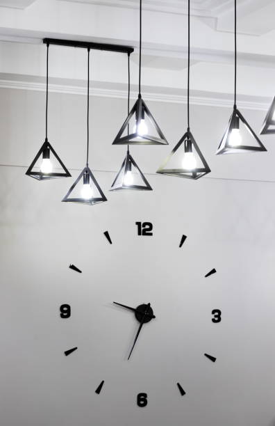 istock Minimalistic design of a wall clock with black numbers and a light bulb 1345447398
