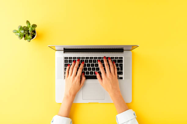 istock Female hands working on laptop. Modern office desktop with small succulent on yellow background with copyspace. Top view 1345449735