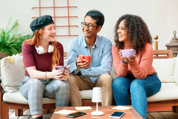 tre diversi giovani amici che si godono un caffè insieme su un divano - coffee couple italy drinking foto e immagini stock