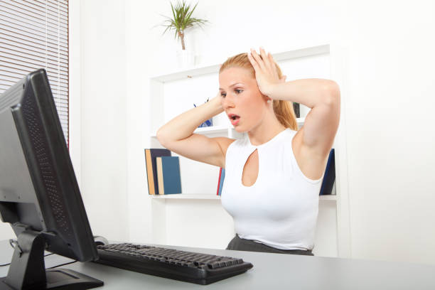 Young woman reacts to what she sees on her computer screen in a darkened room.