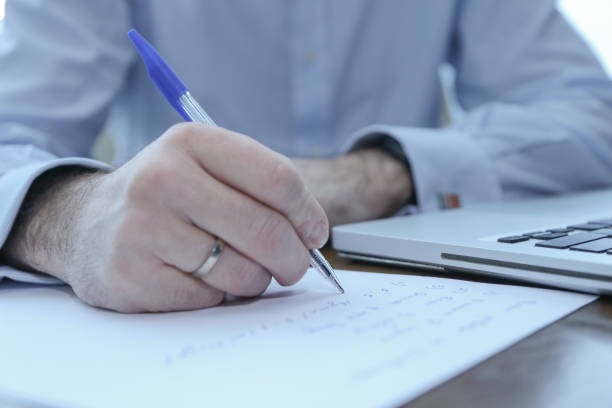 istock A man writes with a pen on a sheet of paper, visible computer 1345454638