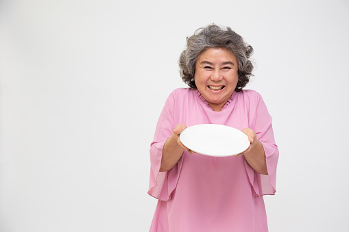 Senior Asian woman holding empty white plate or dish isolated on white background