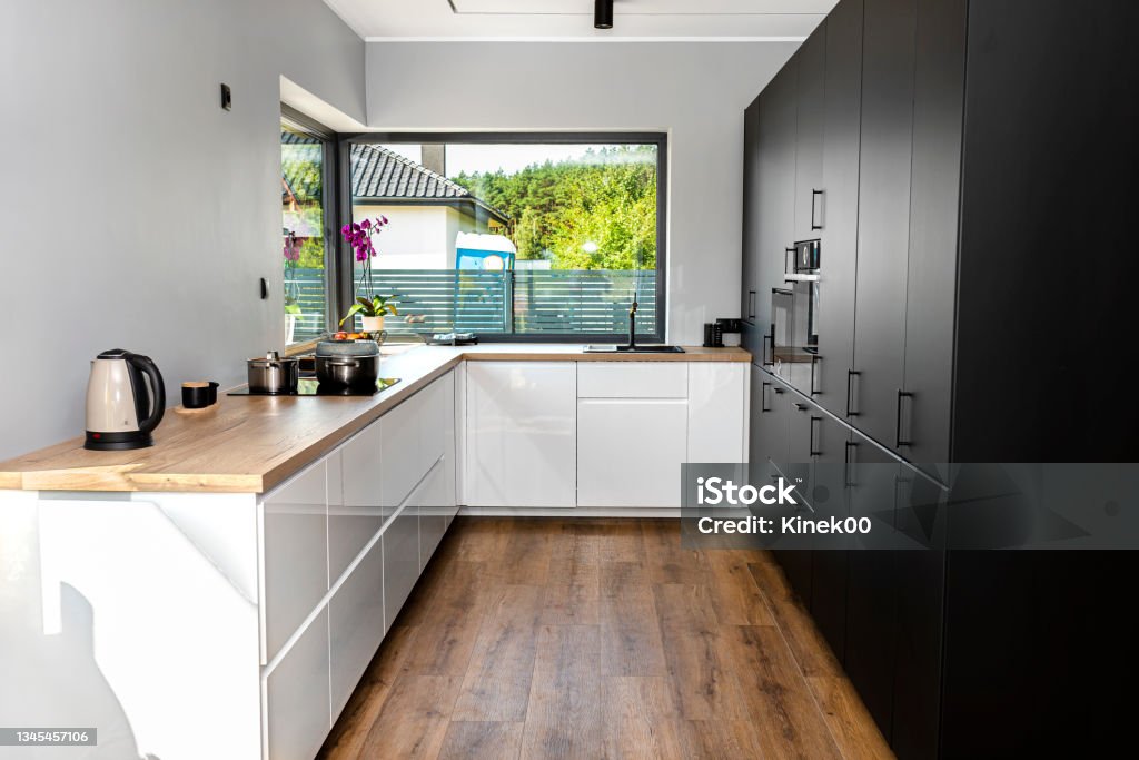 Una cocina moderna con frentes blancos y negros y una gran ventana de esquina, paneles de vinilo en el piso. - Foto de stock de Interior libre de derechos