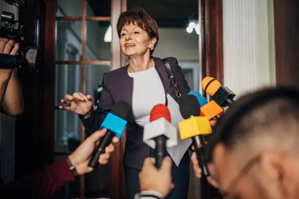 One woman, female politician confronted by journalists with microphones.