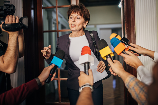 One woman, female politician confronted by journalists with microphones.