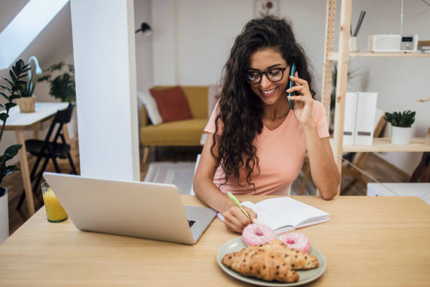 istock Happy young woman working from home and making a phone call 1345462281