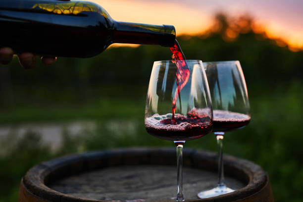 Pouring red wine into glasses on the barrel Pouring red wine into glasses on the barrel at dusk cabernet sauvignon grape stock pictures, royalty-free photos & images