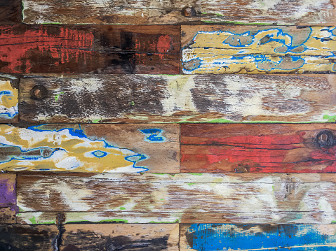 Close-up shot of multi colored paint on rustic timber plank. Some color on the plank are already getting peeled off. The red and blue color is apparent.