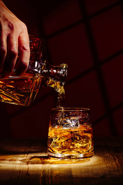 Pouring a glass of whiskey on ice Pouring a glass of whisky with ice from a decanter, in a dark background. scotch whisky stock pictures, royalty-free photos & images