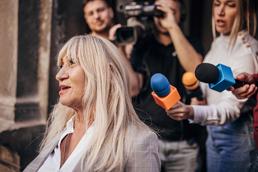Group of people, female politician confronted by journalists with microphones.