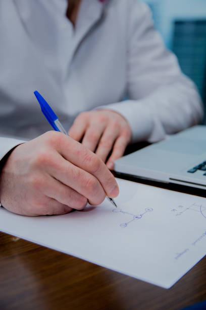 istock A man writes with a pen on a sheet of paper, visible computer 1345469622