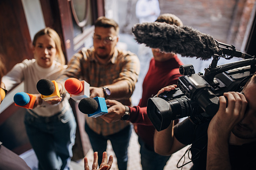 Female journalist at news conference, recording notes, holding microphone and smarthopne lice dictaphone