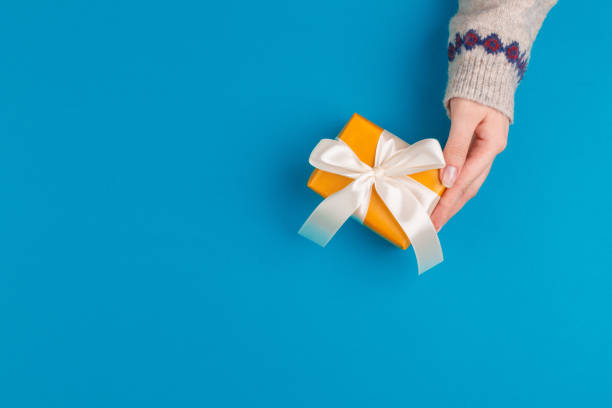 istock Small gift box in female hands on blue background, view from above 1345476154