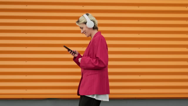 Cute woman in urban background walking and listening to music with headphones.