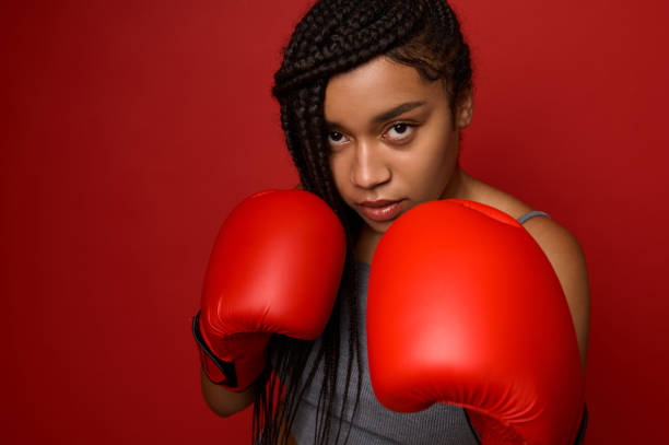 портрет крупным планом концентрированной молодой африканской спортивной женщины-боксера в красных боксерских перчатках, делающей прямой  - muay thai audio стоковые фото и изображения
