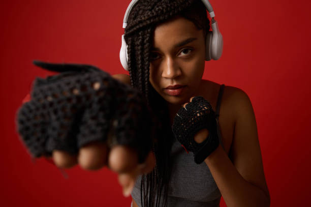 close-up de jovem africana concentrada boxeadora atlética em fones de ouvido e luvas vermelhas de boxe fazendo um chute reto, isolado no fundo de cores com espaço de cópia. contato conceito de arte marcial - muay thai audio - fotografias e filmes do acervo