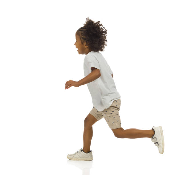 Happy small black boy in shorts and shirt is running. Side view. Full length, isolated. stock photo