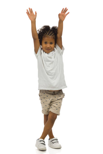 Small black boy in shorts and shirt is standing with arms raised. Full length, isolated. stock photo