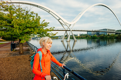 Mature woman on the promenade early morning with her bicycle pausing to view the Infinity Bridge at Stockton on Tees, England.