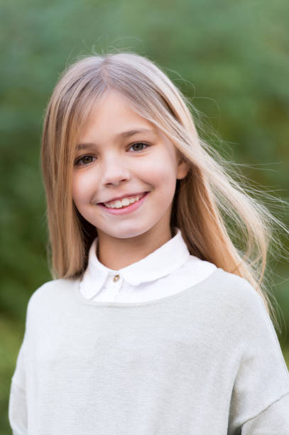Child in grey sweater on idyllic autumn day. Girl with blond long hair smile on natural landscape. Happy childhood concept. Beauty, youth, growth. Kid fashion and style.