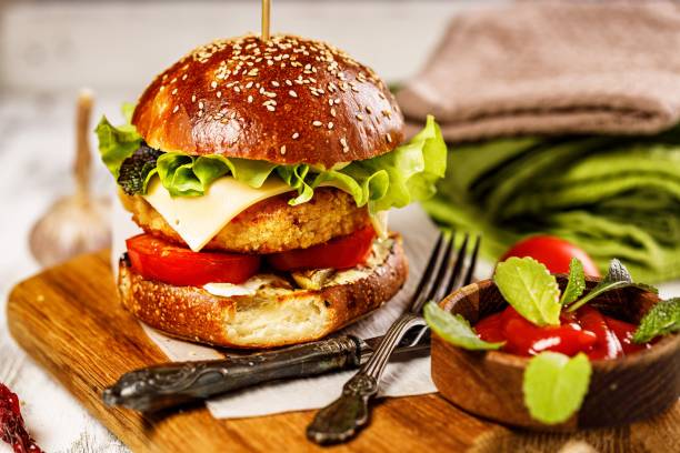 istock Homemade appetizing chicken burger with cheese, fresh salad and vegetables on a cutting board. Fresh lettuce leaves, tomatoes and onions. Traditional American food. White rustic background. Close-up 1345480486