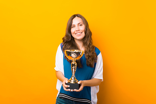 Young proud woman is holding the trophy she has just got over yellow background.