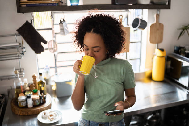 istock Young woman drinking coffee or tea and using a smartphone at home 1345484921
