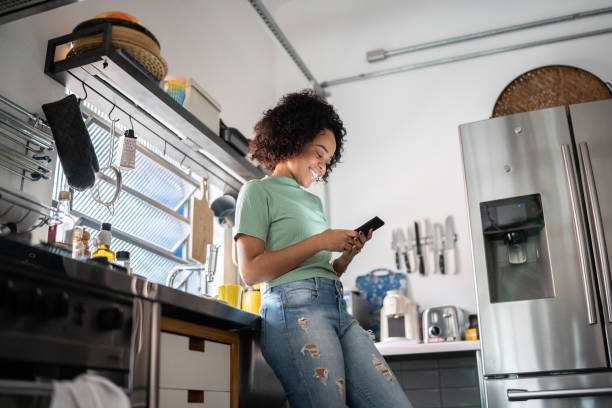 istock Young woman holding a mug and using smartphone at home 1345484949